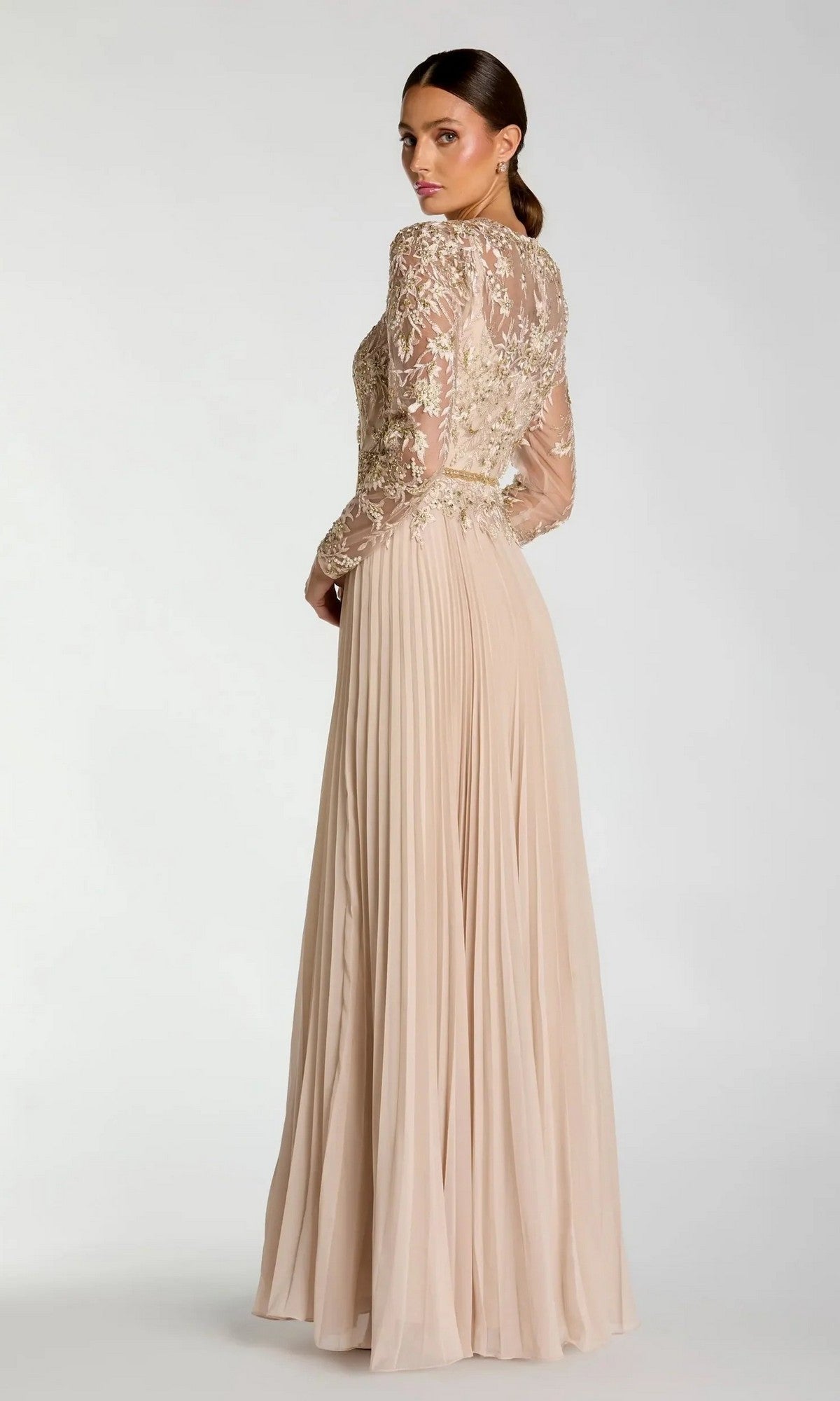 A woman stands against a plain background, wearing the Mac Duggal 11986 long formal dress with sheer lace sleeves and intricate embroidery, looking back over her shoulder.